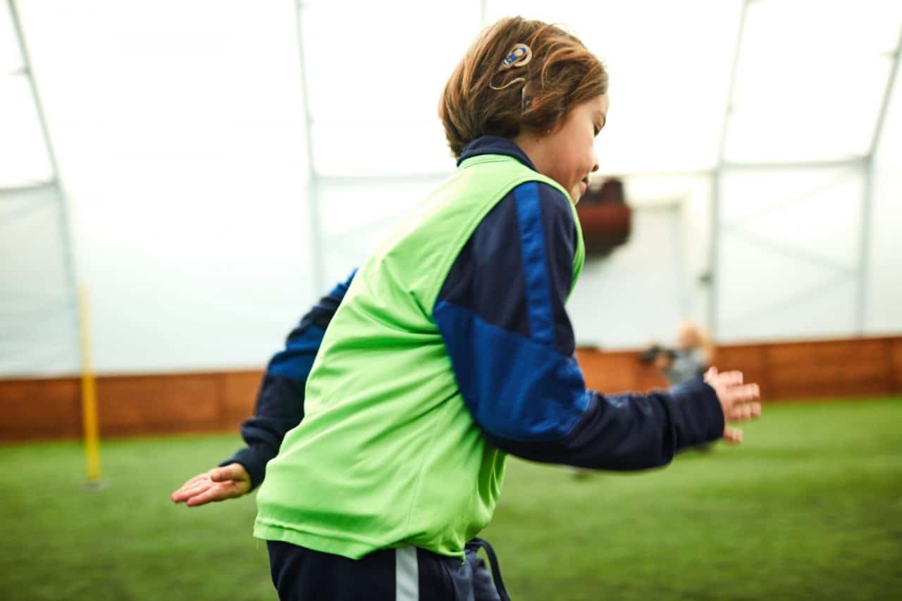 Photo of a child who has a cochlear implant running across a field