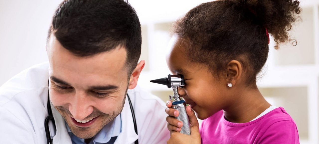 A child looking through an otoscope near a smiling audiologist