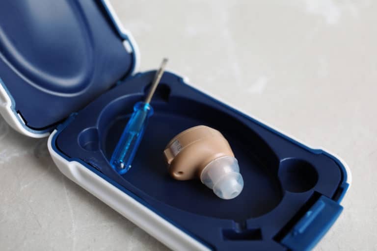 A hearing aid and small screwdriver in an open case