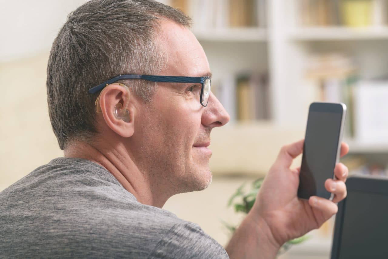 Man with a hearing aid uses his phone.