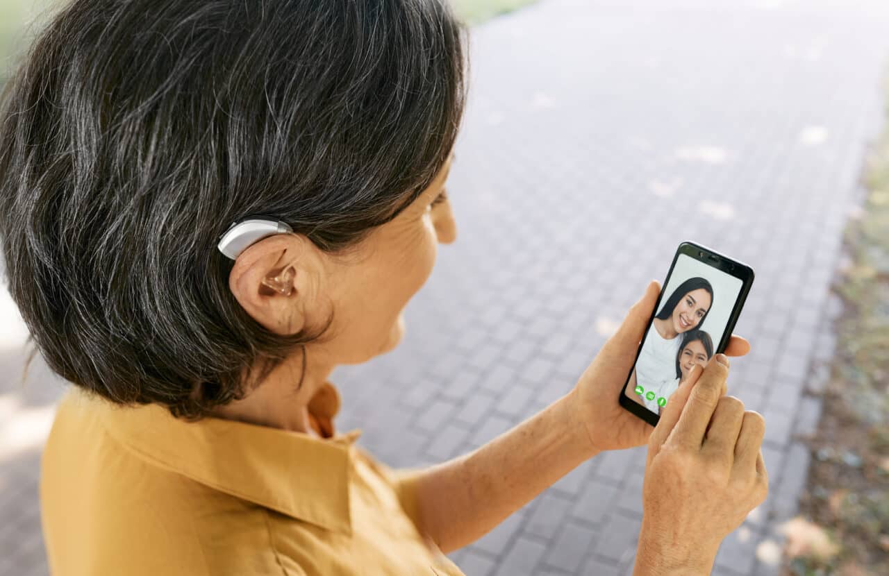 Senior woman with a hearing aid behind the ear communicates with her daughter and granddaughter via video communication via a smartphone. Full human life with hearing aids