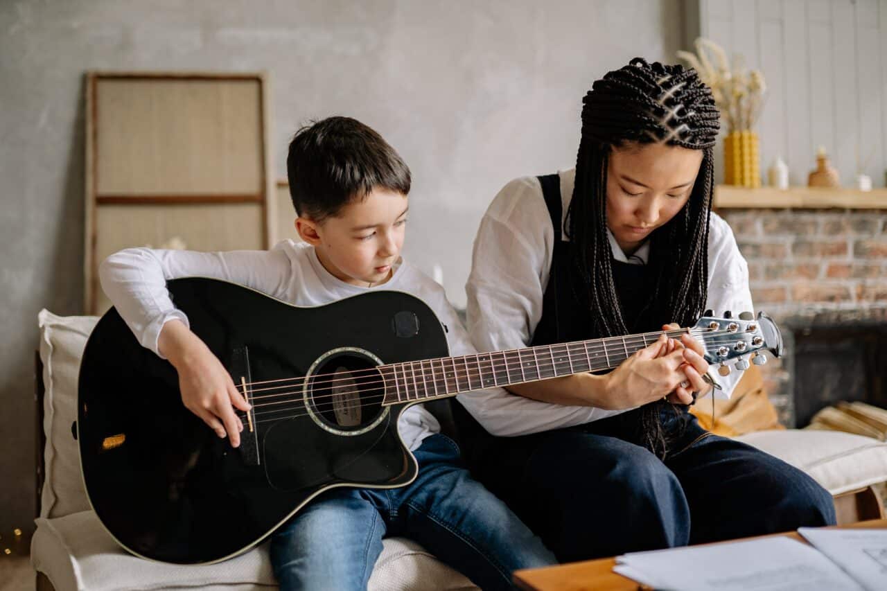 Woman teaches a young boy how to play guitar.