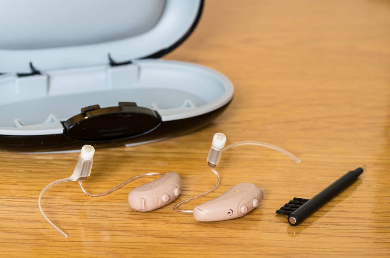 Close up of a pair of tiny modern hearing aid and cleaning brush on bedside table.