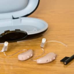 Close up of a pair of tiny modern hearing aid and cleaning brush on bedside table.