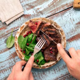 Man eats a beef grilled steak and spinach on wooden table.