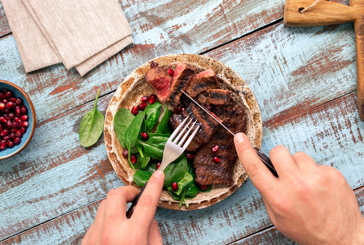 Man eats a beef grilled steak and spinach on wooden table.