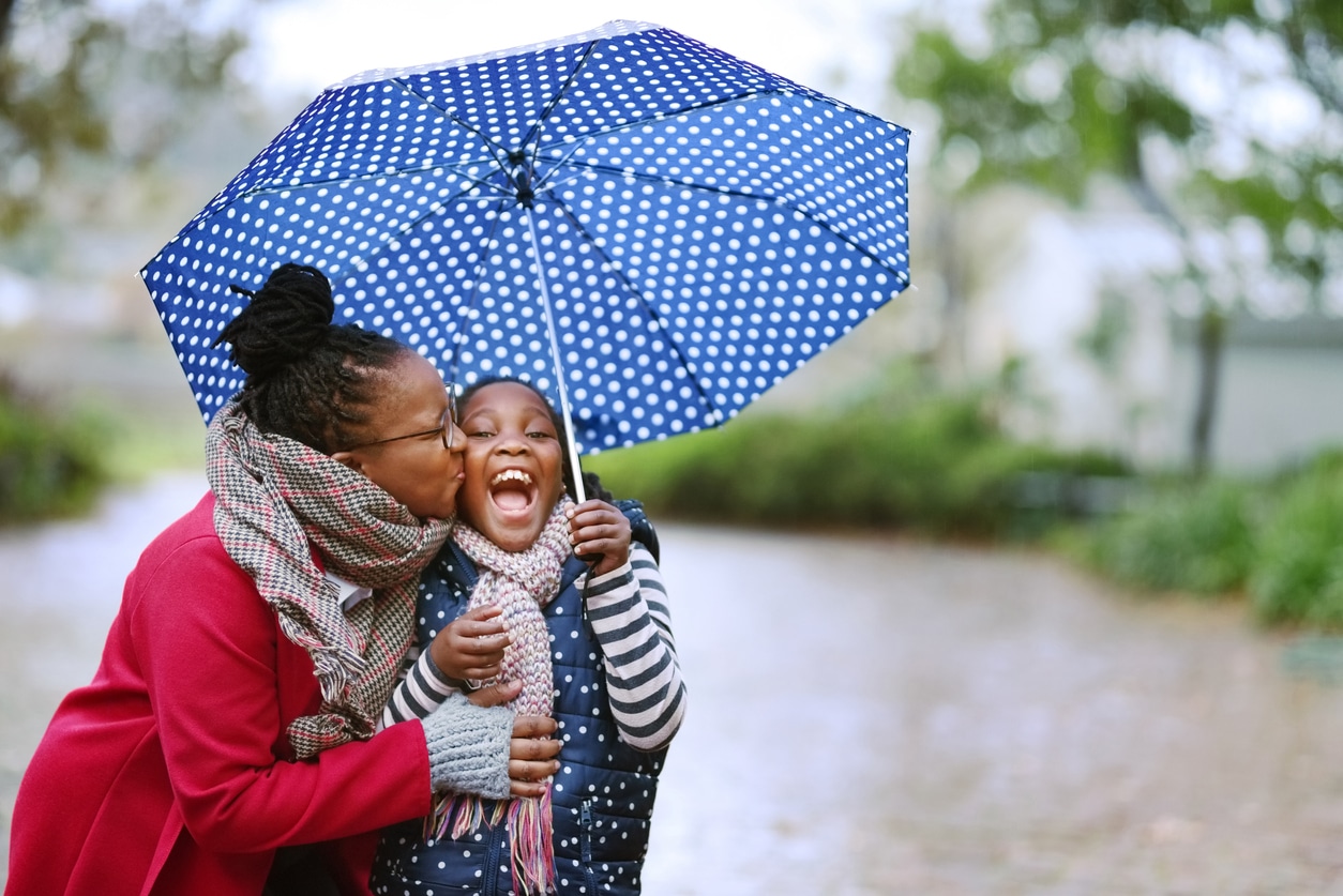 Mother and daughter smiling under an umbrella. 